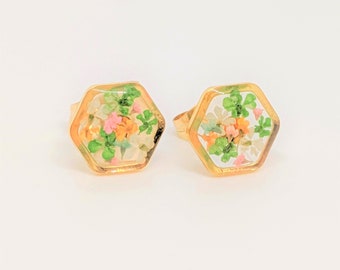 May include: A pair of gold rings with hexagonal settings. Each ring features a clear resin filled with pressed flowers in shades of pink, white, and green.