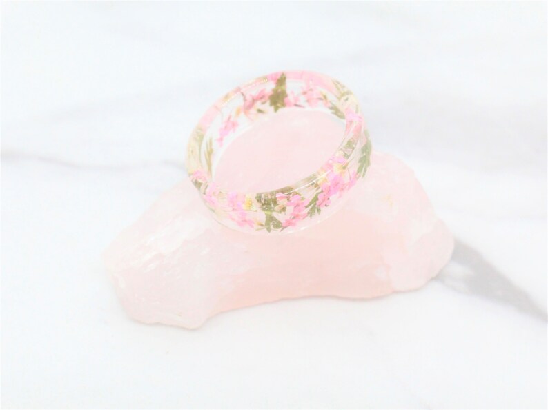 May include: A clear resin ring with pink and green pressed flowers embedded in the resin.