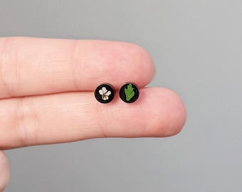 May include: A pair of black stud earrings with a white flower and a green leaf pressed inside the resin.