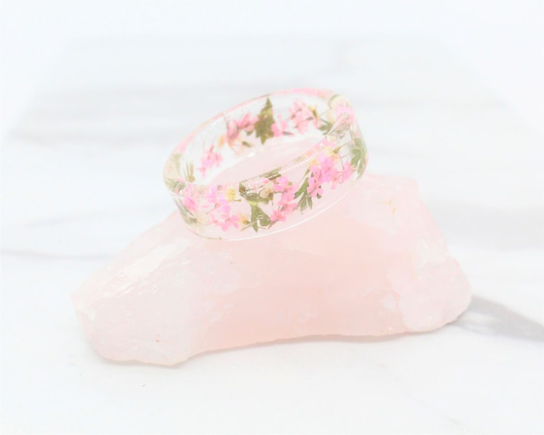 May include: A clear resin ring with pink and green pressed flowers embedded in the resin.