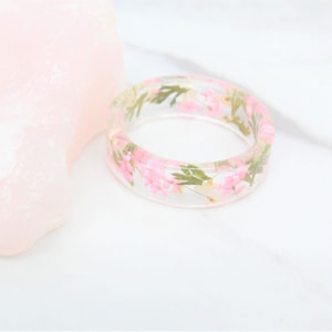 May include: A clear resin ring with pink and white pressed flowers embedded inside.