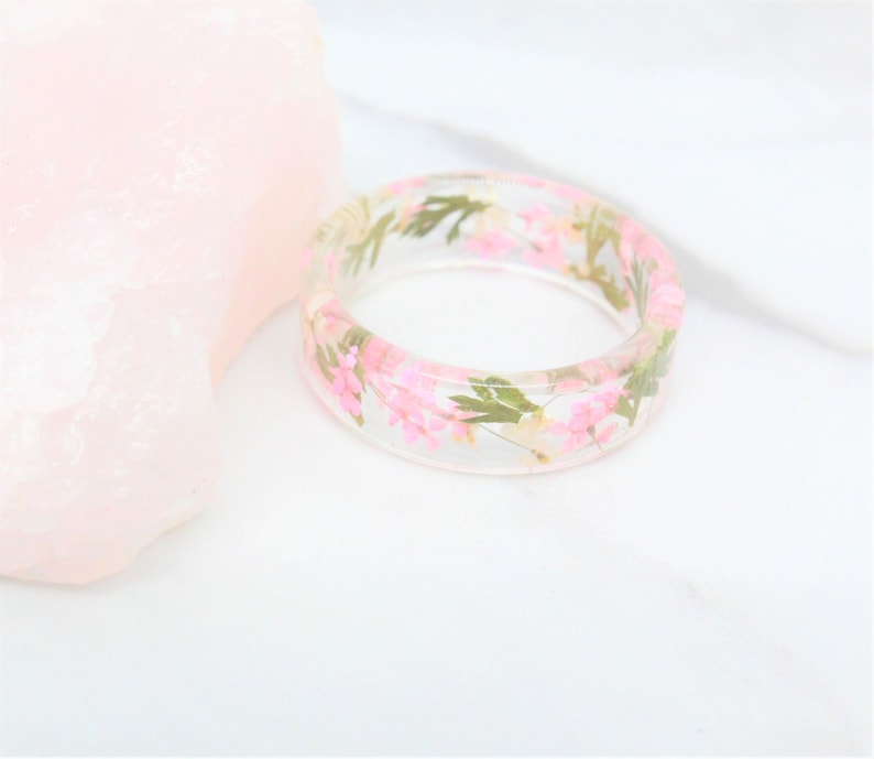 May include: A clear resin ring with pink and white pressed flowers embedded inside.