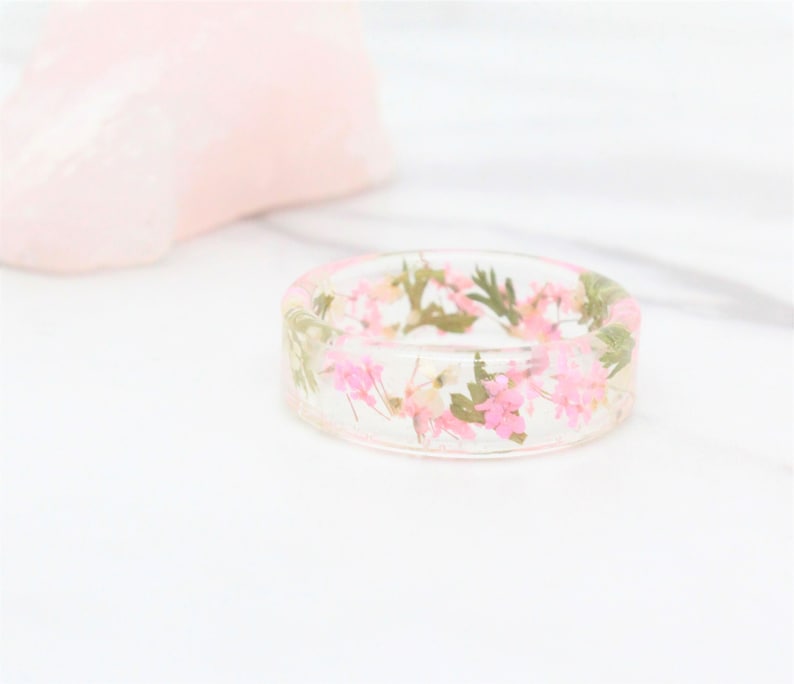 May include: A clear resin ring with pink and green pressed flowers embedded inside.