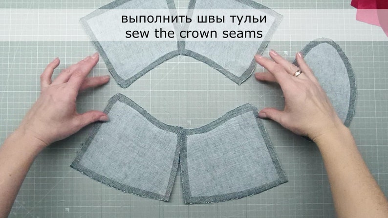 May include: Four gray fabric pieces with a dark gray border, laid out on a gray cutting mat. The text "выполнить швы тульи sew the crown seams" is written in white on a black background at the top of the image.