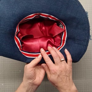 May include: A blue denim hat with a red satin lining and a red, white, and blue ribbon trim.
