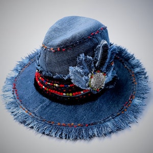 May include: A blue denim hat with a frayed brim and a beaded trim. The hat has a decorative feather and a silver charm.