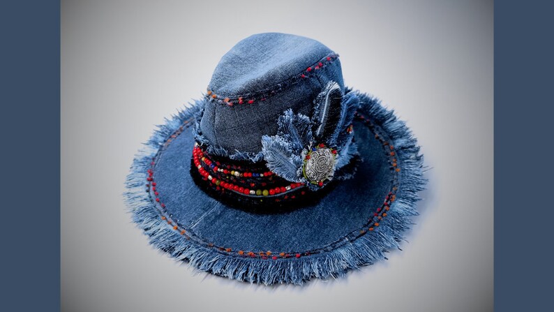 May include: A blue denim hat with a frayed brim and a beaded trim. The hat has a decorative feather and a silver charm.