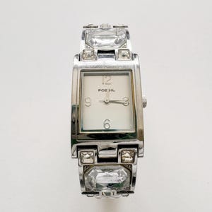 May include: A white ceramic mug with a black handle and the text "But First, Coffee" in a black, bold font. The mug is sitting on a white surface. The mug appears to be 4 inches tall.