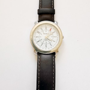 May include: A wristwatch with a white face, silver-colored bezel, and a dark brown leather band. The watch face displays the brand name "Burnsto A" and has black numerals and hands. The band is stitched with a lighter thread.