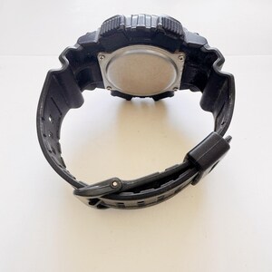 May include: Black digital watch with a textured bezel and band. The watch has a silver-colored back and a black buckle. The watch is designed for sports and outdoor activities.