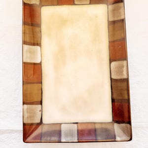May include: A rectangular glass serving tray featuring a large, solid cream-colored center panel surrounded by a wide border of alternating square blocks in shades of deep red, burnt orange, dark brown, and metallic gold with a glossy finish.