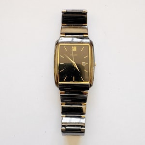 May include: A rectangular Pulsar watch with a black face and gold-tone accents. The watch features a date display and a stainless steel band. The watch face displays the number XII. The watch is a classic accessory.