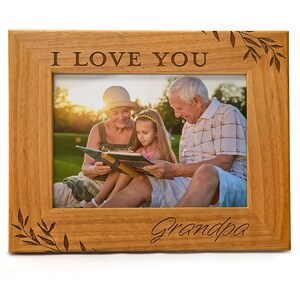 May include: A wooden picture frame with a photo of a family reading a book together. The frame has the words "I Love You Grandpa" engraved on it.