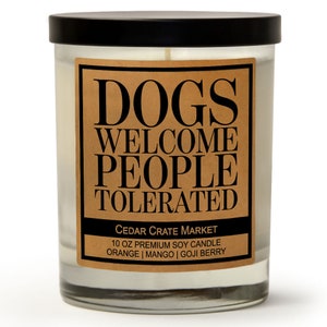 K&ouml;nnte beinhalten: Ein klares Glasgef&auml;&szlig; f&uuml;r eine Kerze mit einem schwarzen Deckel und einem braunen Etikett mit der Aufschrift "DOGS WELCOME PEOPLE TOLERATED CEDAR CRATE MARKET 10 OZ PREMIUM SOY CANDLE ORANGE | MANGO | GOJI BERRY".