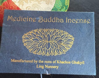 Può includere: Un sacchetto di carta blu con lettere dorate che recitano "Medicine Buddha Incense" e "Manufactured by the nuns of Khachoe Ghakyil Ling Nunnery". Un disegno di fiore di loto dorato si trova al centro del sacchetto.