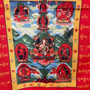 May include: A colourful Tibetan Buddhist Thangka painting depicting a deity surrounded by other figures. The painting is framed in gold and red and features a blue sky with white clouds. The painting is set against a red background with Tibetan script.