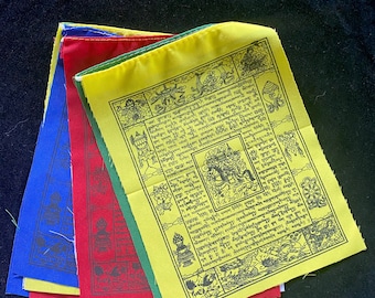 May include: A stack of colorful prayer flags with Tibetan script and symbols. The flags are yellow, green, red, blue, and white. The flags are made of fabric and have a traditional design.