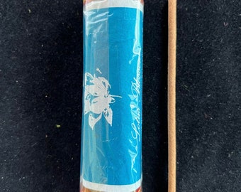Può includere: Un pacchetto di bastoncini di incenso avvolti in cellophane blu con un disegno di farfalla e il testo "Lotus Blossom". Un singolo bastoncino di incenso è mostrato accanto al pacchetto.