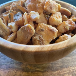 May include: A wooden bowl filled with small, irregular pieces of amber resin. The amber is a light yellow to orange colour and has a translucent appearance.