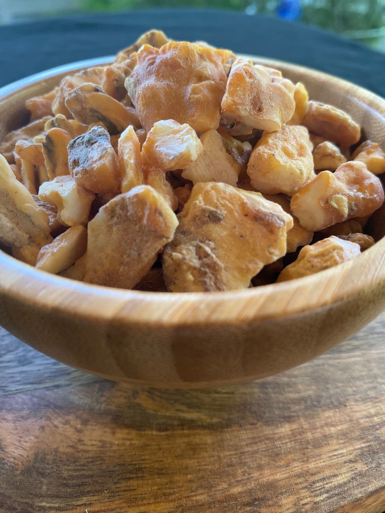 May include: A wooden bowl filled with small, irregular pieces of amber resin. The amber is a light yellow to orange colour and has a translucent appearance.
