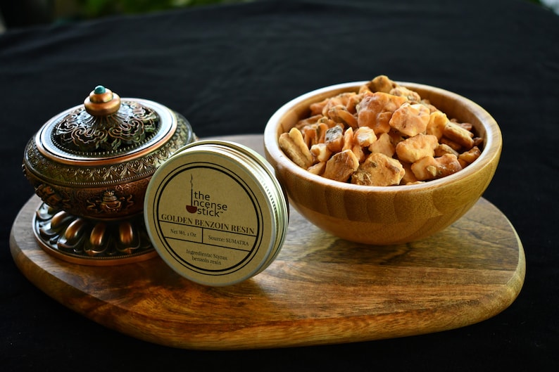 May include: A small tin container of golden benzoin resin from Sumatra, labelled "The Incense Stick Golden Benzoin Resin". The resin is also shown in a wooden bowl.