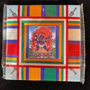 Puede incluir: Una bandera de oración tibetana colorida con una imagen enmarcada de una deidad en el centro. La bandera está hecha de seda y tiene una variedad de colores, incluyendo rojo, amarillo, verde, azul y blanco. La imagen de la deidad está rodeada por un borde rojo y dorado.