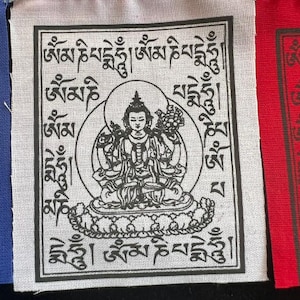 May include: A string of prayer flags with a central square featuring a detailed black and white illustration of a seated figure within a circle. The square is surrounded by Tibetan script. The flags are in blue, white, and red.