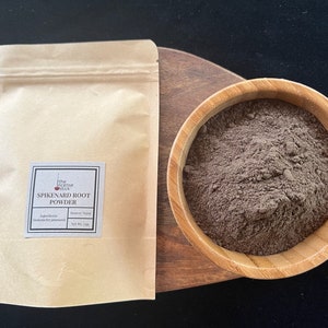 May include: A brown paper bag with a label that reads "The Incense Stick: Spikenard Root Powder". The bag is next to a wooden bowl filled with a dark brown powder.