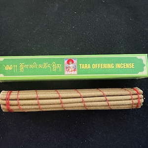 May include: A green box of Tara Offering Incense with text in English and another language. A bundle of incense sticks is tied with red string. The incense sticks are light brown.