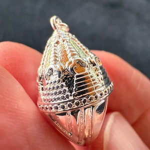 May include: Silver pendant in the shape of a dome with intricate details and a textured surface.
