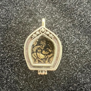 May include: A silver pendant with a hinged opening, revealing a gold-toned image of a deity inside. The pendant has intricate details and a decorative design.