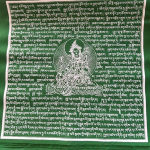 May include: Green fabric prayer flag with white text and a white image of a deity. The text includes the words "Tara" and "Om".