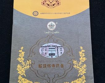 Può includere: Una scatola dorata con sfondo grigio e bordo dorato. La scatola contiene un'immagine di un edificio con il testo "敏珠林寺药香" in lettere dorate. Il testo "Minzhu Monastery Inc." è anche in lettere dorate.
