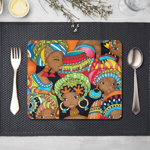 Puede incluir: Un mantel individual rectangular con una colorida ilustración de mujeres con pañuelos en la cabeza y joyas. La obra de arte utiliza una paleta de naranja, verde, azul y rojo. El mantel individual está sobre una superficie gris oscuro, con un tenedor y una cuchara.