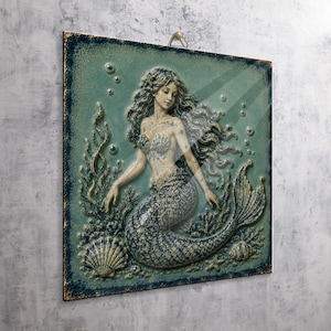 May include: A square wall plaque featuring a relief sculpture of a mermaid with long flowing hair, surrounded by underwater elements including seaweed, bubbles, and seashells. The artwork is finished in shades of teal, blue, and cream.
