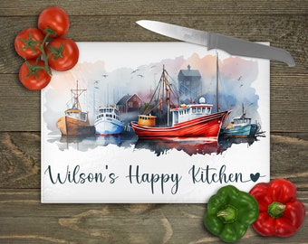 May include: A rectangular glass cutting board with a watercolor painting of fishing boats in a harbor. The text "Wilson's Happy Kitchen" is printed on the board. Red tomatoes, green and red bell peppers, and a knife are on the wooden surface.
