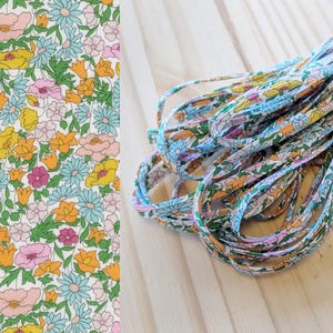 May include: Floral patterned fabric and matching shoelaces. The fabric features a repeating pattern of colorful flowers in shades of pink, yellow, blue, and orange on a white background. The shoelaces are a similar floral pattern.
