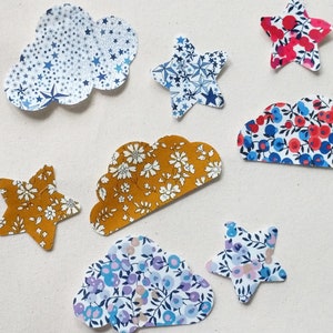 Puede incluir: Un conjunto de aplicaciones de tela en forma de nubes y estrellas. Las nubes están en varios patrones florales, y las estrellas están en azul y blanco, rojo y blanco, y amarillo y blanco con patrones florales.