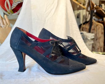 May include: A pair of black suede high-heeled shoes with mesh panels and red accents. The shoes have a pointed toe and a lace-up design.
