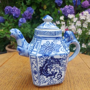 Op de afbeelding: Een blauw-witte keramische theepot met een drakenontwerp. De theepot heeft een zeshoekige vorm, een deksel en een handvat. De tuit is gevormd als een kameelkop. De theepot is versierd met bloemen en geometrische patronen.