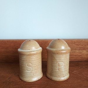 May include: A pair of ceramic salt and pepper shakers. The shakers are beige with a speckled finish and a rounded top. The letter "S" is embossed on one shaker, and the letter "P" is embossed on the other.