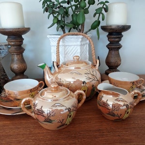May include: A vintage Japanese tea set with a gold and brown floral design. The set includes a teapot, creamer, sugar bowl, and two teacups and saucers.
