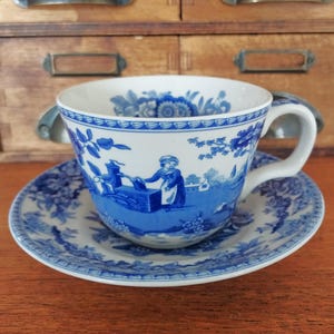 Op de afbeelding: Een blauw en wit porseleinen theekopje en schotelset met een bloemenpatroon en een scène van een vrouw die water uit een put haalt.