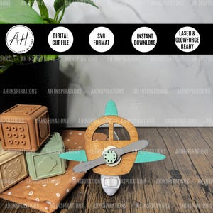 May include: A wooden aeroplane night light with a teal propeller and a light switch on the bottom. The aeroplane is painted brown with a teal accent on the nose and wings. The night light is sitting on a wooden surface with a brown and white patterned fabric in the background.