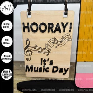 May include: A wooden sign with the text "HOORAY! It's Music Day" in black lettering. The sign also features a treble clef and musical notes.