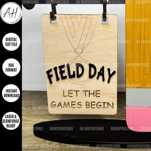 May include: A wooden sign with a medal design and the text "Field Day Let The Games Begin".