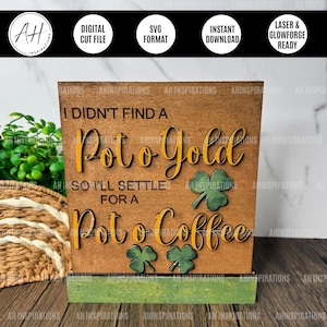 Może przedstawiać: Drewniany znak z tekstem "I didn't find a pot o' gold so I'll settle for a pot o' coffee". Znak jest ozdobiony zielonymi koniczynkami i ma rustykalne brązowe wykończenie.