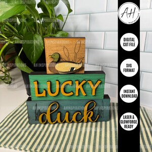 Puede incluir: Decoración de madera con temática de patos con una ilustración de pato y la palabra "LUCKY" en amarillo. El diseño incluye un bloque de madera con la palabra "duck" en amarillo. La imagen también incluye texto: "DIGITAL CUT FILE", "SVG FORMAT", "INSTANT DOWNLOAD" y "LASER & GLOWFORGE READY".
