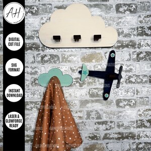 May include: A wooden cloud-shaped coat rack with three hooks and a blue and white airplane design. The rack is mounted on a brick wall.