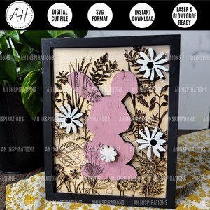 May include: A pink bunny rabbit silhouette with floral details, surrounded by white flowers and greenery, is laser cut from wood and framed in black. The image is labelled "AH Inspirations".